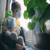 Un enfant avec un masque ayant un peluche dans les bras regarde par la fenetre