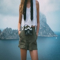 Une photographe avec une caméra autour du cou portant une blouse blanche et un short