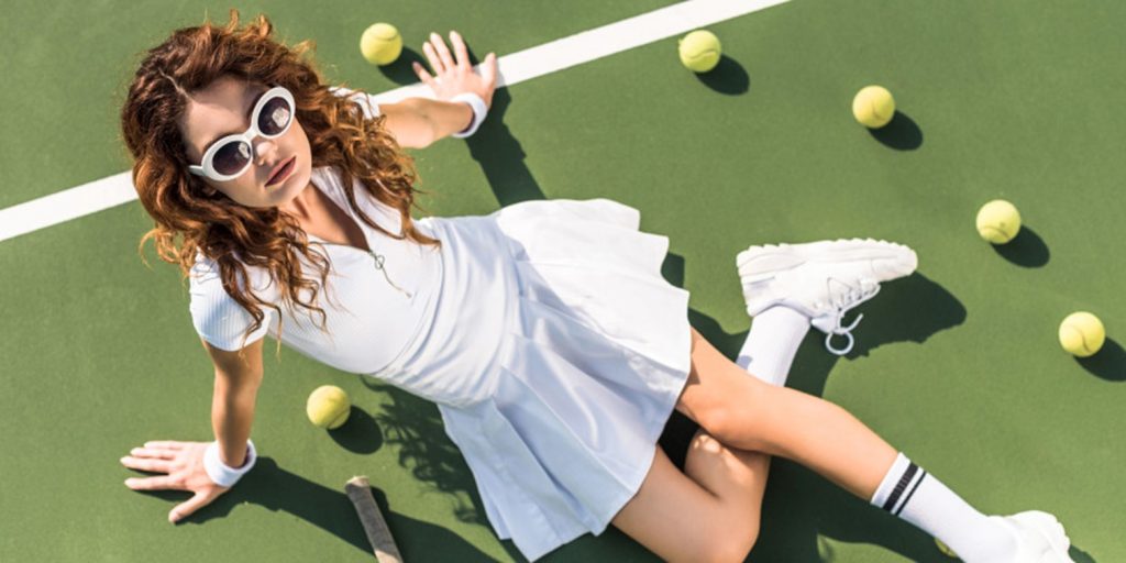 Une jeune femme posant en tenue tenniscore sur un court de tennis 