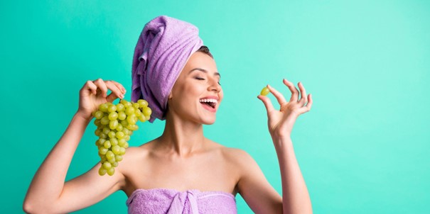 Une jeune femme en serviette qui tient une grappe de raisin