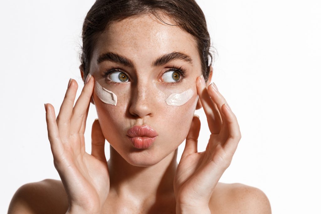 Une jeune femme qui etale de la creme sur son visage en faisant du bone tapping