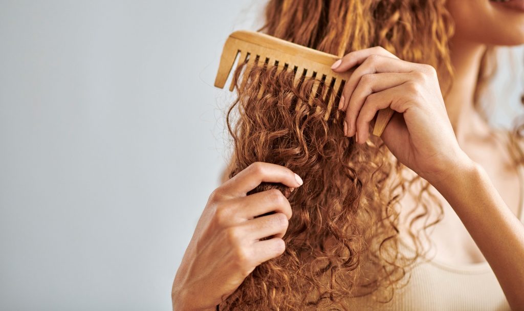 Une personne aux cheveux boucles qui se brosse avec un peigne à larges dents 