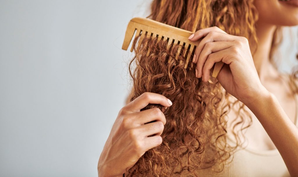 Une personne aux cheveux boucles qui se brosse avec un peigne à larges dents