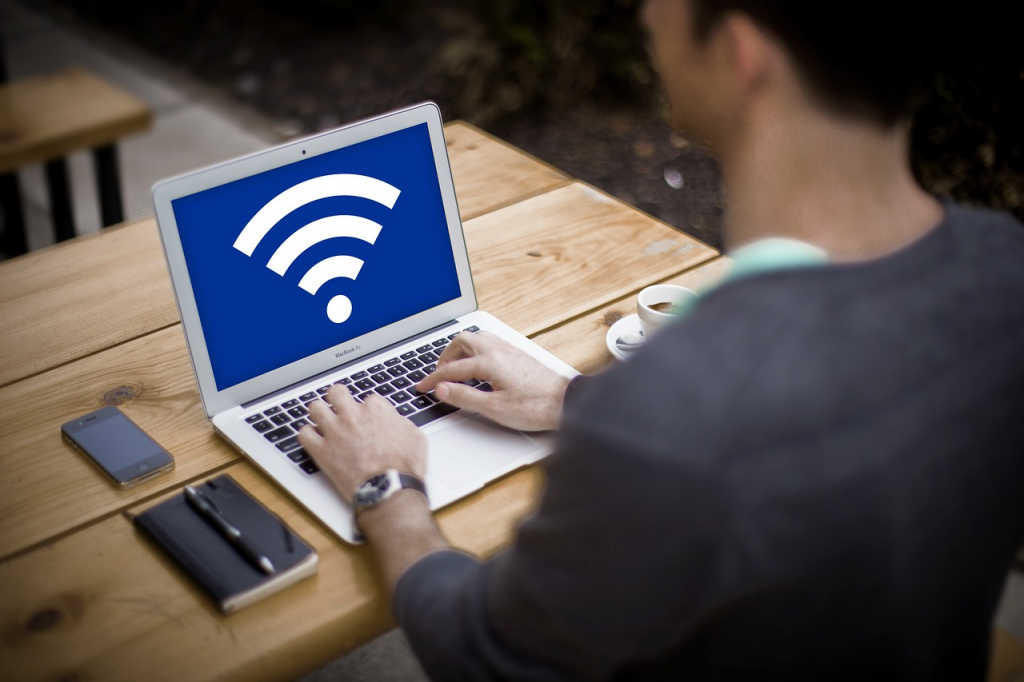 Un homme en train de travailler sur son PC portable, dans un lieu public avec l’icône Wi-Fi affiché sur son écran.