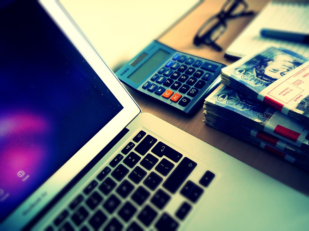 Un ordinateur portable avec des billets et une calculatrice posée à côté.
